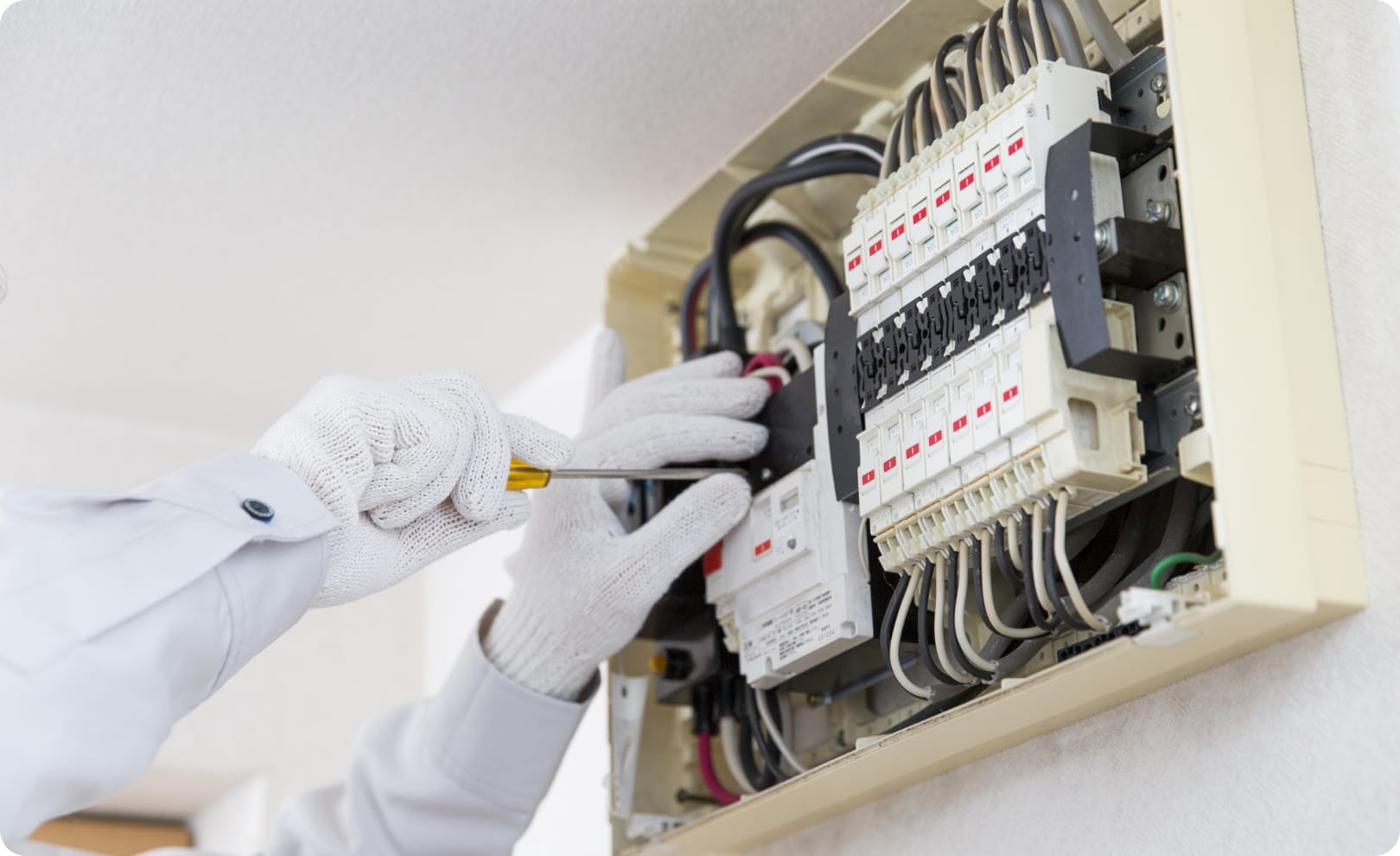 作業員が分電盤の内部を点検・整備している様子で、工具と手袋を使用している